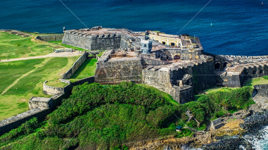 A historic fort and lighthouse beside blue waters, Old San Juan, Puerto Rico Aerial Stock Photo AX101_026.0000000F | Axiom Images