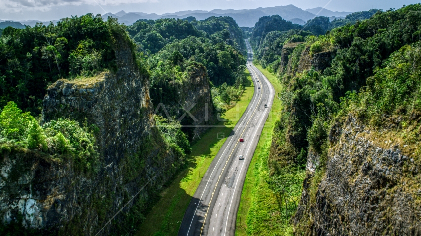 Light traffic on a highway through lush green mountains, Karst Forest, Puerto Rico Aerial Stock Photo AX101_084.0000123F | Axiom Images