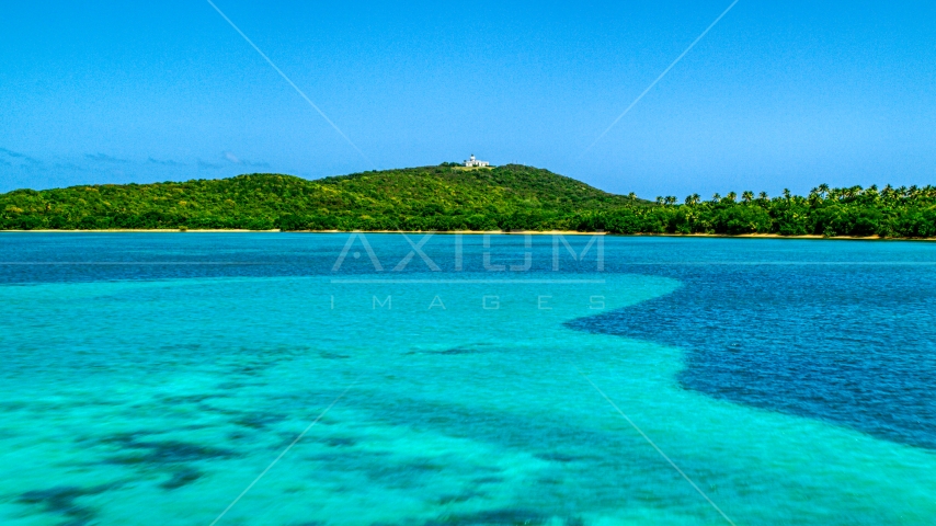 A view across crystal clear blue water of Cape San Juan Light, Puerto Rico Aerial Stock Photo AX102_060.0000000F | Axiom Images