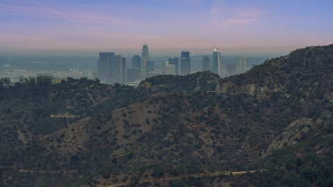 AX0158_004.0000052 - Aerial stock photo of Downtown Los Angeles seen from behind a hill, twilight, California