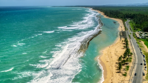 AX102_018.0000143F - Aerial stock photo of Waves rolling toward the beach and highway, Loiza, Puerto Rico