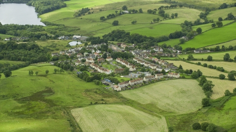 AX109_003.0000251F - Aerial stock photo of Rural homes surrounded by green fields in the village of Banton, Scotland