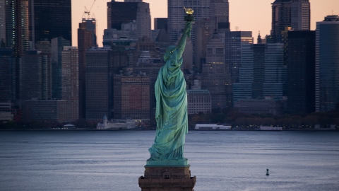 AX118_045.0000075F - Aerial stock photo of Statue of Liberty and Lower Manhattan skyscrapers at sunrise, New York