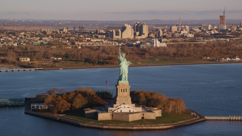 AX118_144.0000175F - Aerial stock photo of Statue of Liberty at sunrise in New York, with Jersey City in the background