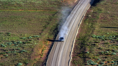 AX138_223.0000115 - Aerial stock photo of Silver SUV trailing a plume of dust on a desert road, Moab, Utah