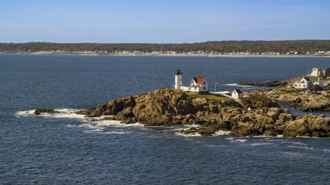 AX147_238.0000188 - Aerial stock photo of Cape Neddick Light, coastal town in background, autumn, York, Maine