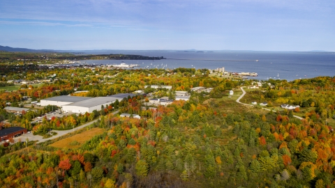 AX148_076.0000028 - Aerial stock photo of A forest near warehouse buildings and small coastal town, autumn, Rockland, Maine