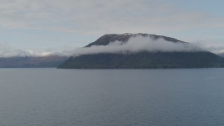 AK0001_0430 - 4K aerial stock footage fly by forested cloud covered peak, from over bay, Prince William Sound, Alaska