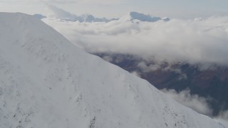 4K aerial stock footage rounding snowy summit, reveal cloud covered Kenai Mountains, Alaska Aerial Stock Footage | AK0001_0528