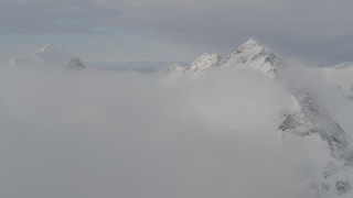 4K aerial stock footage flying by a snow covered peak, low clouds, Chugach Mountains, Alaska Aerial Stock Footage | AK0001_0561