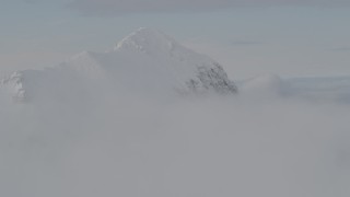 4K aerial stock footage flying by snow covered peak, surrounded by clouds, Chugach Mountains, Alaska Aerial Stock Footage | AK0001_0562