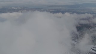 4K aerial stock footage flying over snowy ridge, low clouds, reveal Anchorage, Chugach Mountains, Alaska Aerial Stock Footage | AK0001_0566