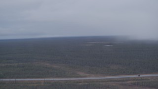 AK0001_1019 - 4K aerial stock footage flying by forest during a rain storm to reveal a highway in the Alaskan Wilderness