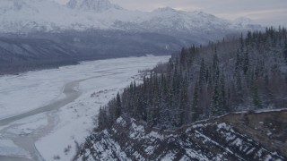 AK0001_1086 - 4K aerial stock footage flying over snow covered, tree lined cliffs following Matanuska River, Alaska