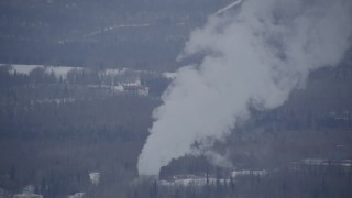 AK0001_1150 - 4K aerial stock footage a power plant, tilting up in plumes of steam, Anchorage, Alaska in snow