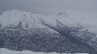 4K aerial stock footage flying over snowy summit revealing wooded valley, Chugach Mountains, Alaska Aerial Stock Footage | AK0001_1174