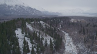 AK0001_1224 - 4K aerial stock footage following a river next to snow covered, wooded hills, Knik River Valley, Alaska