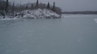 4K aerial stock footage following a river past a snow covered, wooded hill, Knik River Valley, Alaska Aerial Stock Footage | AK0001_1266