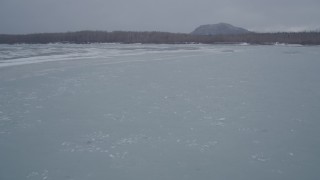 4K aerial stock footage following an icy river towar wooded, snowy riverbank, Knik River Valley, Alaska Aerial Stock Footage | AK0001_1271