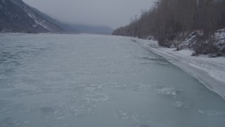 AK0001_1273 - 4K aerial stock footage following the snowy, wooded riverbank of an icy river, Butte, Alaska