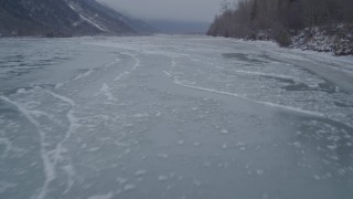 AK0001_1274 - 4K aerial stock footage following wooded, snow covered riverbank of icy river, Butte, Alaska