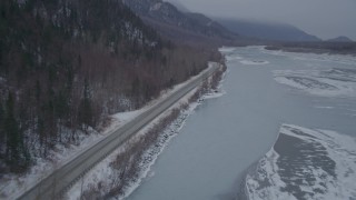 AK0001_1278 - 4K aerial stock footage following Old Glenn Highway next to an icy river and snow, Butte, Alaska