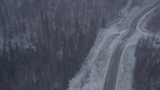 4K aerial stock footage flying over forest to Glenn Highway through falling snow, Eagle River, Alaska Aerial Stock Footage | AK0001_1309