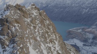 AK0001_1353 - 4K aerial stock footage flying over a rocky, snow covered peak revealing Eklutna Lake, Alaska