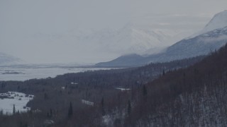 AK0001_1578 - 4K aerial stock footage descending along snowy, wooded slope on rim of Knik River Valley, Alaska