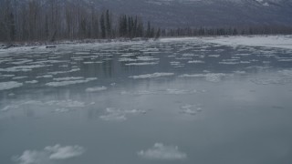 4K aerial stock footage flying low over icy river toward snow covered shore, Knik River Valley, Alaska Aerial Stock Footage | AK0001_1604