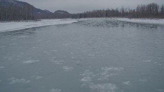 4K aerial stock footage flying low over icy river toward snow covered shore, Knik River Valley, Alaska Aerial Stock Footage | AK0001_1607