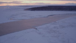 AK0001_1699 - 4K aerial stock footage flying over a river toward a forest at twilight, Point MacKenzie, Alaska in snow