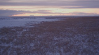 4K aerial stock footage flying low over frozen, snowy ground and grass at twilight, Point MacKenzie, Alaska Aerial Stock Footage | AK0001_1701