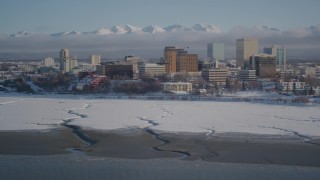 AK0001_2023 - 4K aerial stock footage tilt up from surface of Cook Inlet revealing snowy Downtown Anchorage, Alaska