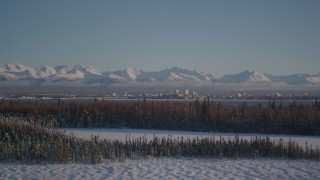 AK0001_2038 - 4K aerial stock footage cloudy Chugach Mountains, snowy forest, Downtown Anchorage, Alaska