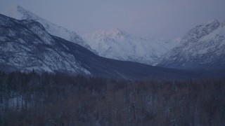 AK0001_2113 - 4K aerial stock footage flying by snowy, forested hills, snowy Talkeetna Mountains at twilight, Alaska