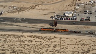 AX0006_053 - Aerial stock footage of 5K aerial  video approach a train running by the town of Mojave in California