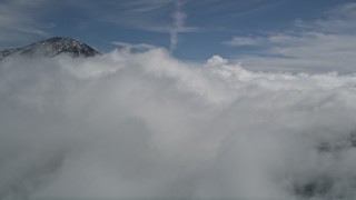 AX0009_093 - 5K aerial stock footage video of thick clouds by a snowy peak in the San Bernardino Mountains in winter, California