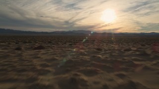 AX0012_039E - 5K aerial stock footage fly low over desert plain toward the sun, Mojave Desert, California