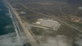 5K aerial stock footage approach and tilt to Camp Pendleton by the coast, seen through the clouds, California Aerial Stock Footage | AX0016_023