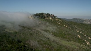 AX0016_056E - 5K aerial stock footage approach fog rolling over a hill near hillside homes, Laguna Niguel, California