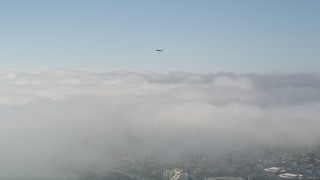 AX0016_080 - 5K aerial stock footage track a jet airliner ascending over clouds, Newport Beach, California