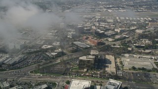 5K aerial stock footage tilt down to office buildings on MacArthur Boulevard, seen through misty clouds, Newport Beach, California Aerial Stock Footage | AX0016_081