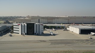 AX0016_114 - 5K aerial stock footage of C-17 Globemaster hanger and smaller hangars with civilian jets at Long Beach Airport, California