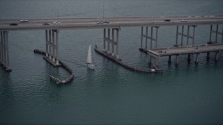 AX0022_073E - 5K aerial stock footage of sailing boat under a bridge on the Rickenbacker Causeway at sunset in Florida