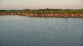 AX0028_027 - 5K aerial stock footage of flying low over water, approaching mangroves and flying over at sunset, Islamorada, Florida