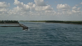 AX0033_040E - 5K aerial stock footage of passing breakwaters and boats sailing through an inlet, Fort Pierce, Florida