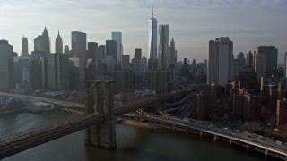 AX0065_0149E - 5K aerial stock footage approach and fly over the Brooklyn Bridge with view of the Lower Manhattan skyline, New York City, winter