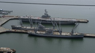 6K aerial stock footage of passing an aircraft carrier and Naval ships docked in Alameda, California Aerial Stock Footage | AX0175_0217