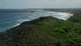 AX101_154E - 4.8K aerial stock footage flying over blue waters toward the beach and tree lined coast, Arecibo, Puerto Rico